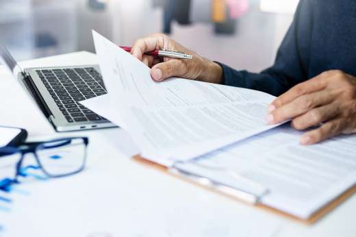 Foto: Person mit Dokumenten und Laptop